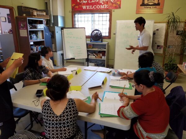 Teacher standing the front of the classroom teaching a small class of students.